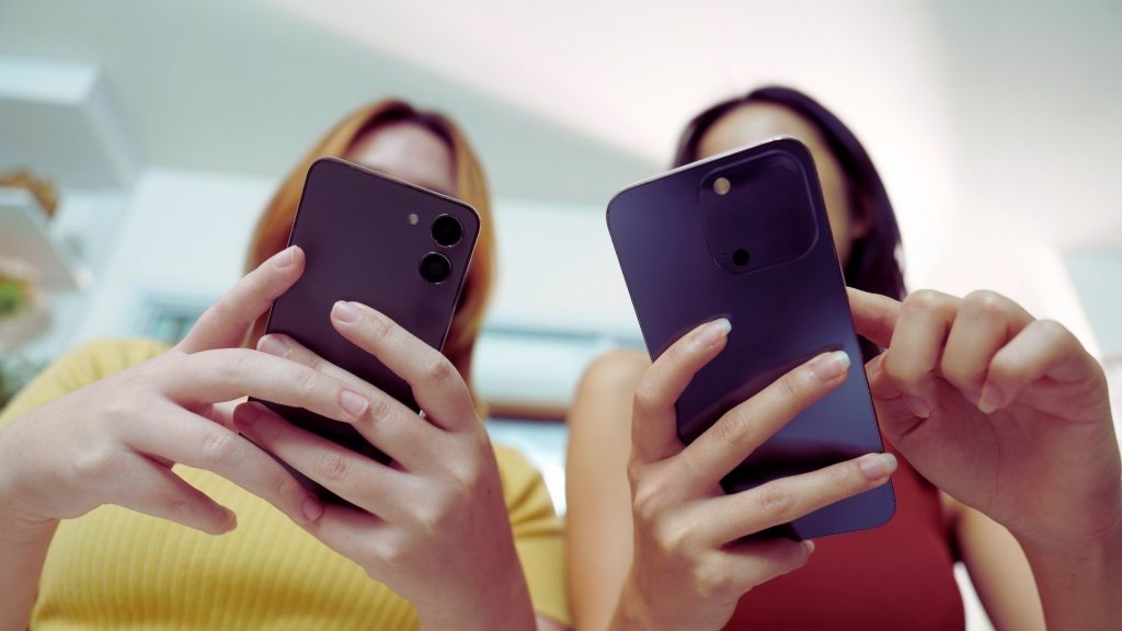 Two teens using smartphones together, representing online influence and peer behavior